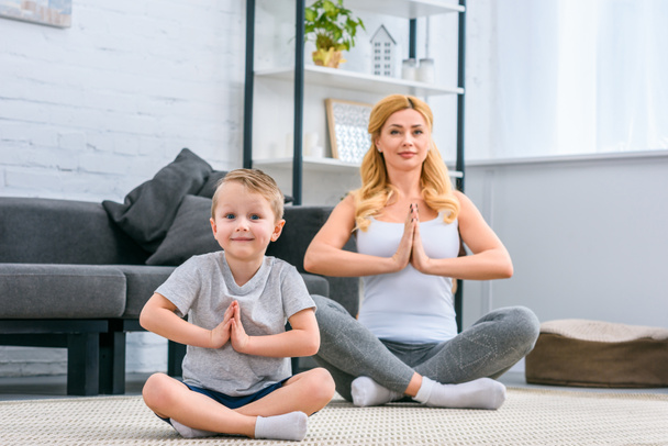 Madre con hijo pequeño practicando yoga en posición de loto en salón
 - Foto, Imagen
