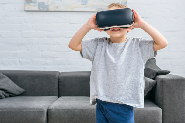 Little boy using virtual reality headset in front of sofa  - Foto, afbeelding