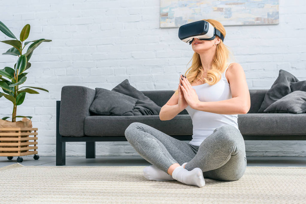 Fiatal nő gyakorló jóga a lótusz helyzet, és használja a virtuális-valóság sisak  - Fotó, kép