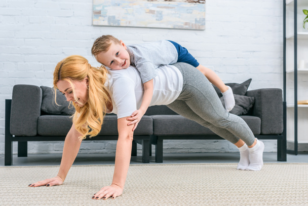 Mutter macht Planke mit kleinem Sohn auf dem Rücken - Foto, Bild