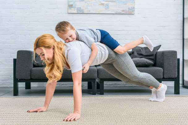 Smiling mother doing plank with little boy on back - Foto, immagini