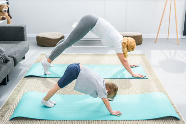 Mother and little boy practicing downward facing dog position on yoga mats - Фото, зображення