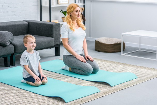 Улыбающиеся мальчик и мать отдыхают на ковриках для йоги
 - Фото, изображение