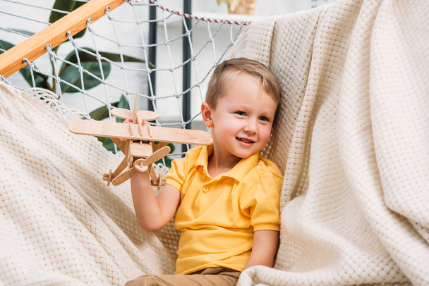 Uśmiechnięty chłopiec bawi się drewniany samolot zabawka w hamaku  - Zdjęcie, obraz