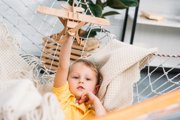 Happy boy playing with wooden airplane toy in hammock  - Photo, Image