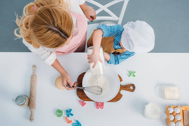 Vista superior de mãe e menino derramando leite em tigela com ovo e farinha
  - Foto, Imagem
