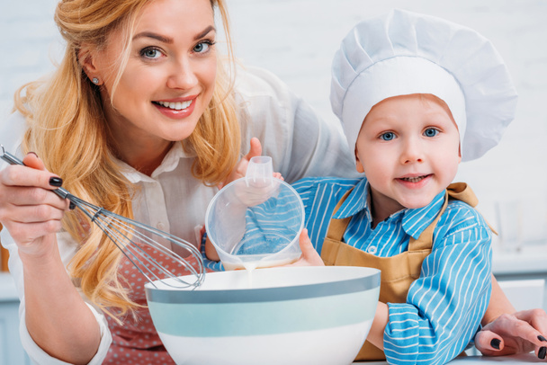 Happy mother with hand beater and little boy pouring milk into bowl - Foto, Bild