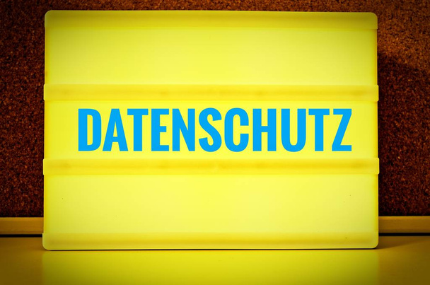 Leuchttafel mit der Aufschrift in deutscher Datenschutzsprache vor einer Pinnwand, in englischer Datenschutzerklärung, in gelb mit hellblauen Buchstaben - Foto, Bild
