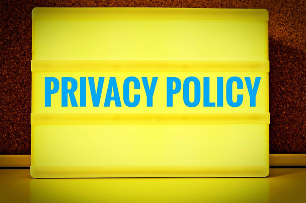 Luminous panel with the inscription in english Privacy Policy in front of a pin board, in german Datenschutzerklaerung, in yellow with light blue letters - Photo, Image