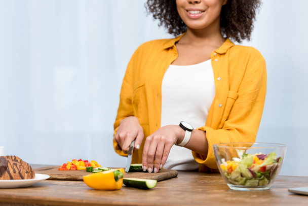 обрізаний знімок усміхненої жінки, що нарізає овочі для салату
 - Фото, зображення
