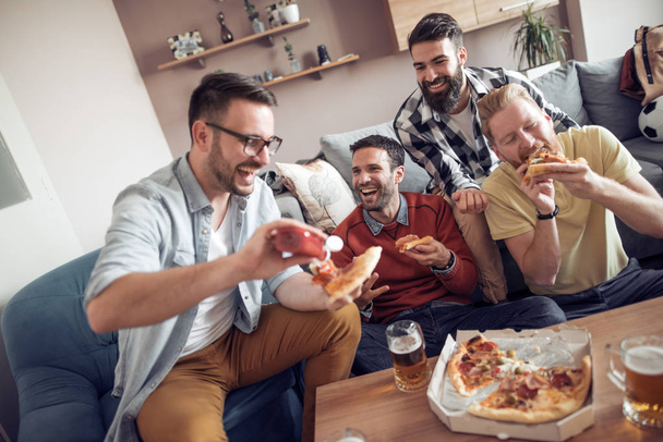 Quattro amici maschi che guardano la TV, mangiano pizza e bevono birra a casa
 - Foto, immagini