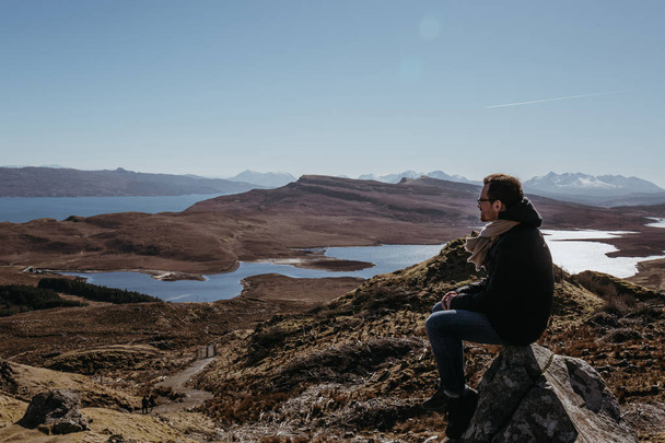 L'uomo che si rilassa sulla cima del Vecchio di Storr passeggiata sull'Isola di Skye, seduto su una pietra, montagne e lago sullo sfondo
.  - Foto, immagini
