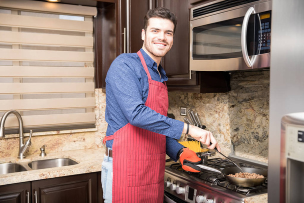 Retrato de un joven hispano guapo en un delantal cocinando el desayuno en casa
 - Foto, imagen