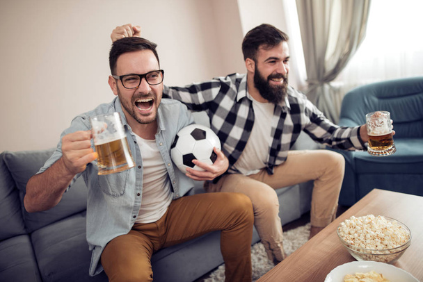 Двоє молодих шанувальників футболу дивляться футбол по телевізору вдома
 - Фото, зображення
