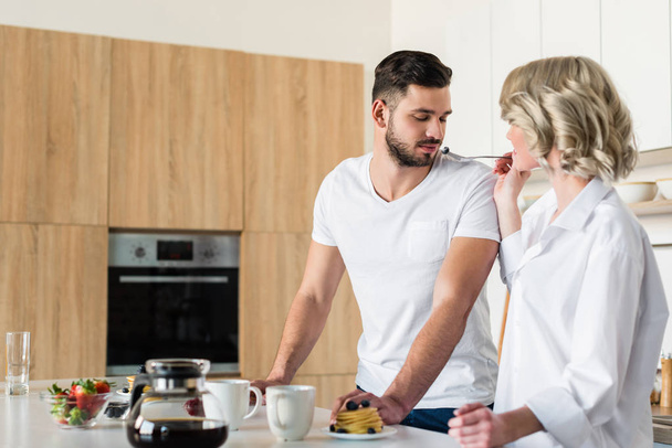 young woman feeding handsome boyfriend at morning in kitchen - Фото, зображення