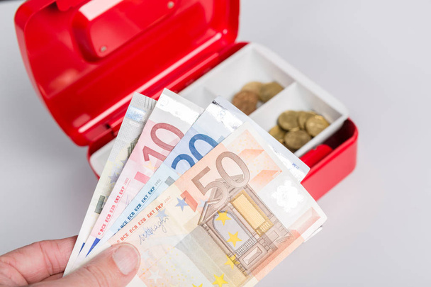 una mano con dinero y una caja de efectivo
 - Foto, imagen
