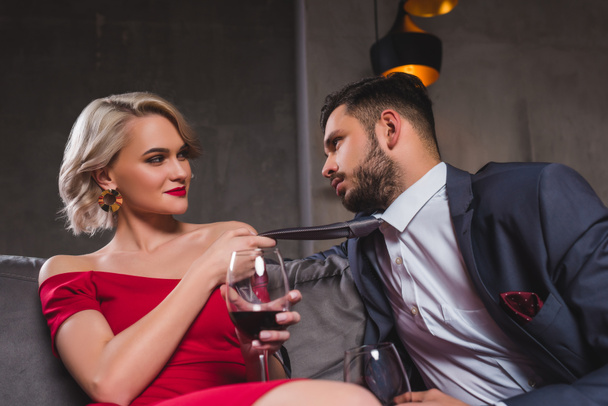 seductive young couple drinking wine, woman holding necktie of handsome boyfriend - Photo, Image