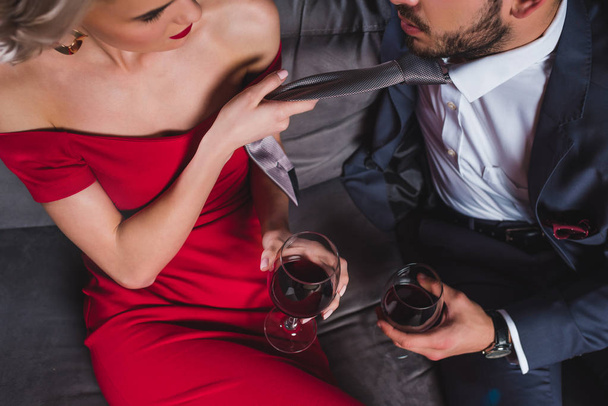 cropped shot of fashionable couple drinking wine, woman holding necktie of handsome boyfriend - Fotó, kép