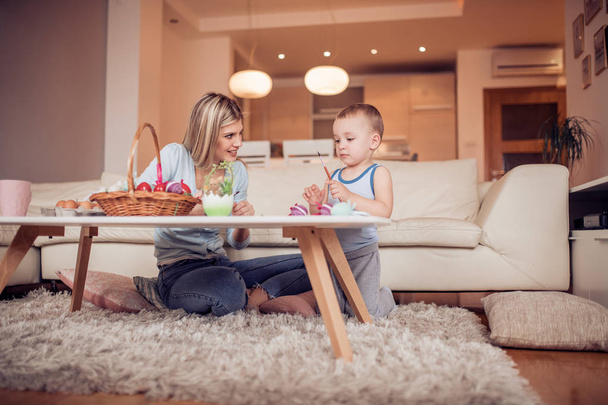 Giovane madre con figlio che dipinge uova di Pasqua in soggiorno
 - Foto, immagini