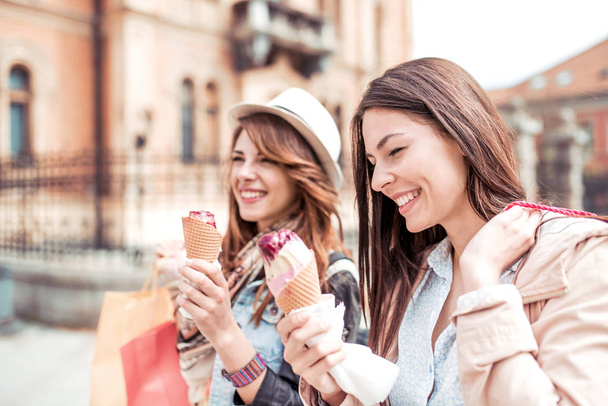 stylish women eating ice cream, talking and smiling while walking after shopping - Φωτογραφία, εικόνα