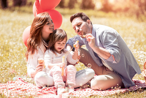 Маленькая девочка с родителями, играющими в парке, пускающими пузыри
 - Фото, изображение
