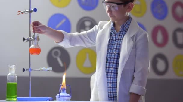 Schoolboy mixes orange liquid in flask in laboratory - Filmati, video