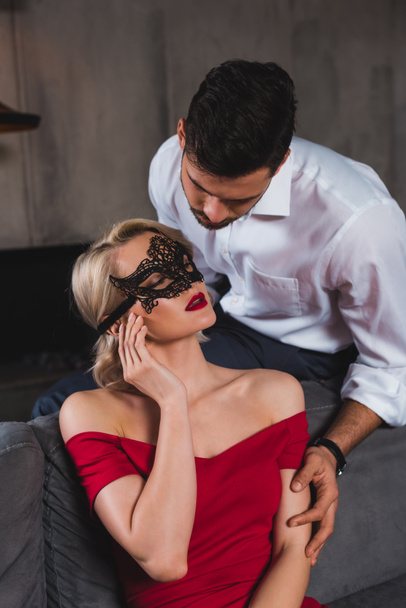 handsome man looking at beautiful sensual woman in red dress and black lace mask - Photo, Image