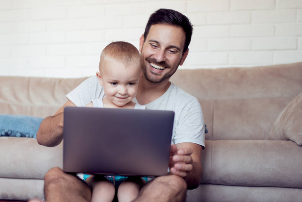 Mladý otec a malý syn procházení laptop doma - Fotografie, Obrázek