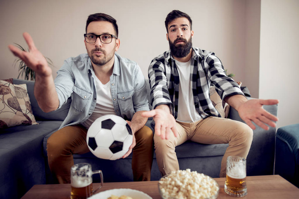 Два молодых футбольных фаната смотрят футбол дома по телевизору
 - Фото, изображение
