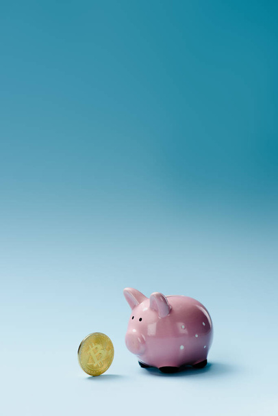 Close up view of pink piggy bank and golden bitcoin on blue backdrop - Fotoğraf, Görsel