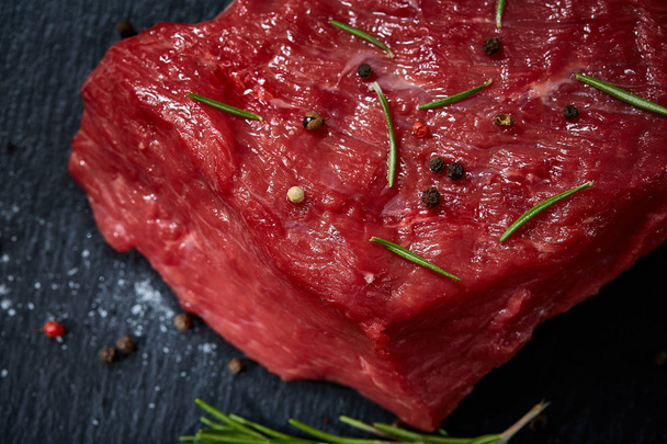 Raw meat beef steaks on black slate board with spices and rosemary over wooden background, copy space - Φωτογραφία, εικόνα