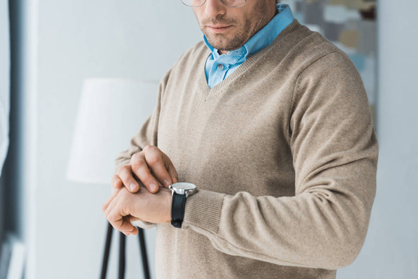Mann mit Brille und lässiger Kleidung schaut auf seine Uhr - Foto, Bild