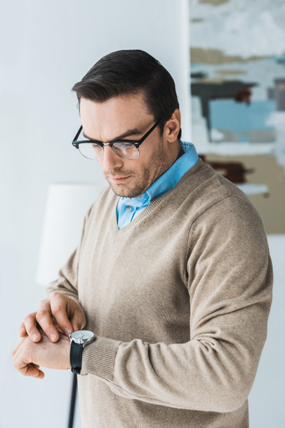 Красивий чоловік в окулярах дивиться на свій годинник
 - Фото, зображення