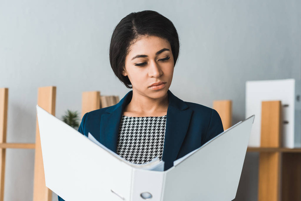 Confident businesswoman looking at folder in modern office - Photo, Image