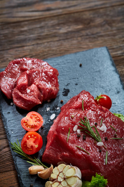 Composition of raw beefsteak on slate board with vegetables and seasoning, selective focus, close-up. - Photo, image