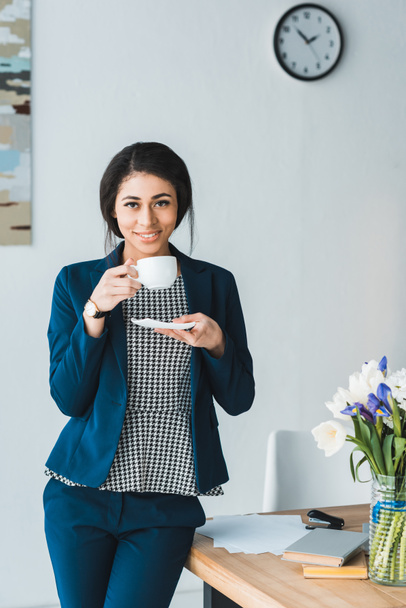 Smiling female manager enjoying coffee during break in modern office - Foto, Bild