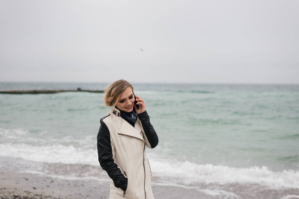 blondi rannalla puhuu puhelimessa ja kallistaa päätään
 - Valokuva, kuva