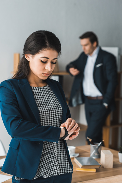 Businesswoman controllo orologio mentre l'uomo in abito da lavoro in piedi da scaffali in ufficio luce
 - Foto, immagini