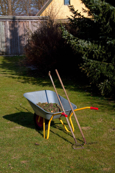 Schubkarre auf der Wiese im Garten mit Harke und Hacke - Foto, Bild