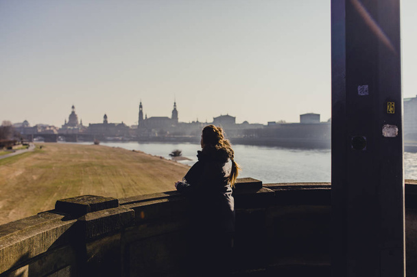young woman on balcony looking at beautiful historical Dresden city with River Elbe at sunset time in Germany  - Photo, Image