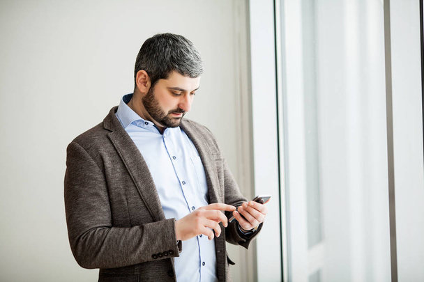 Чоловік тримає телефон - молодий бізнесмен, використовуючи смартфон в офісі
 - Фото, зображення