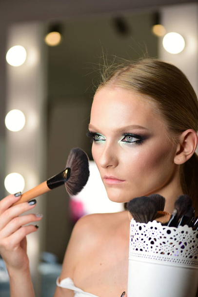 Beautiful young woman applying foundation powder or blush with makeup brush - Фото, изображение