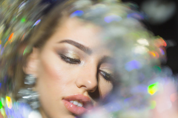 Fashion and art concept. Beauty fashion girl with makeup, lipstick, eyeshadow, mascara, defocused, dark background. View through shimmering brilliant lens. Woman with sensual lips looks sexy. - Photo, Image