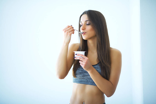 Diet. Happy young woman eating yogurt in kitchen - Photo, Image