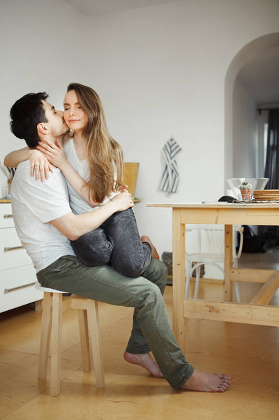 Man kisses woman sitting on his legs in the kitchen. - Foto, imagen