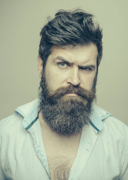 Man with long beard, mustache and stylish hair, light background. Macho on strict face, wears unbuttoned shirt. Barbershop or hairdresser concept. Guy with modern hairstyle visited hairdresser. - Фото, изображение
