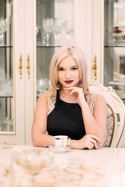 Stylish elegant blonde woman in beauty rich interior, wearing black dress - Zdjęcie, obraz