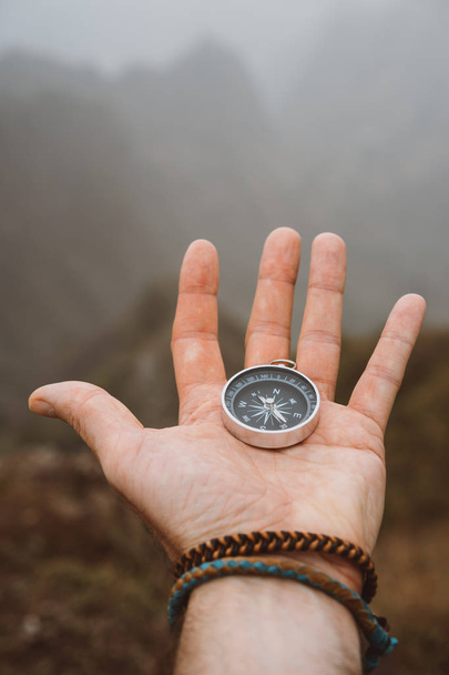 Hand holding a compass. Silhouette of monumental mountain formation in background - Fotografie, Obrázek