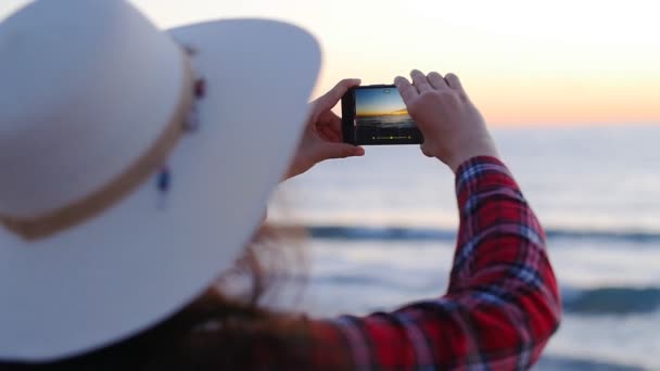 Mujer joven tomando fotos en la playa al atardecer o al amanecer
 - Metraje, vídeo