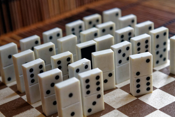 Peças de dominó em uma fileira e um statnd diferente, no fundo de mesa de madeira marrom de bambu
 - Foto, Imagem